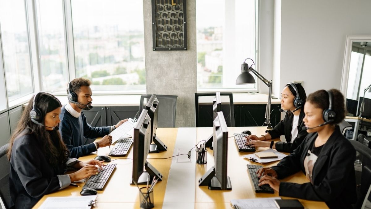 Four individuals working in an open layout office in front of a computer with a headset on