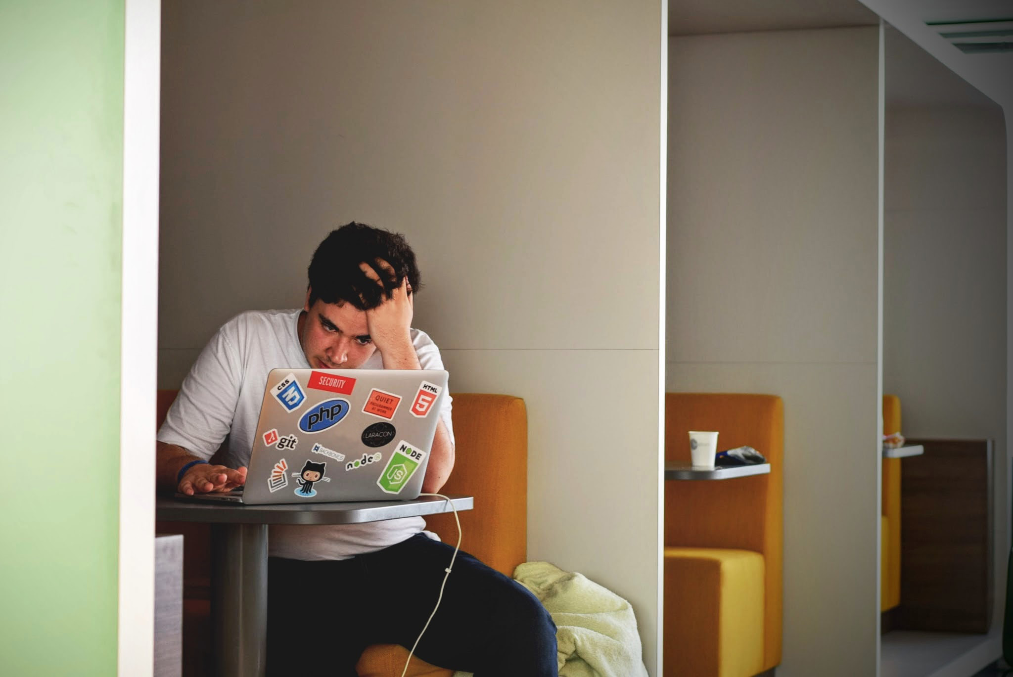 Man sitting at a table in front of a laptop working with one hand on his forehead