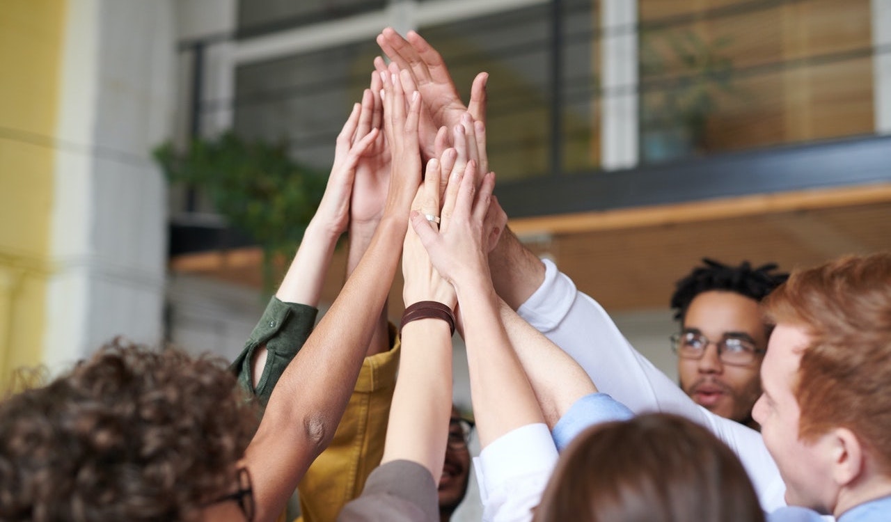 A diverse group of people circling together with the focus on their hands being raised and joined together