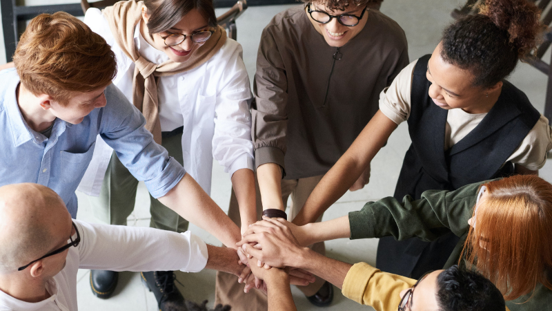 Eight colleagues joining their hands together in the middle of their group circle.